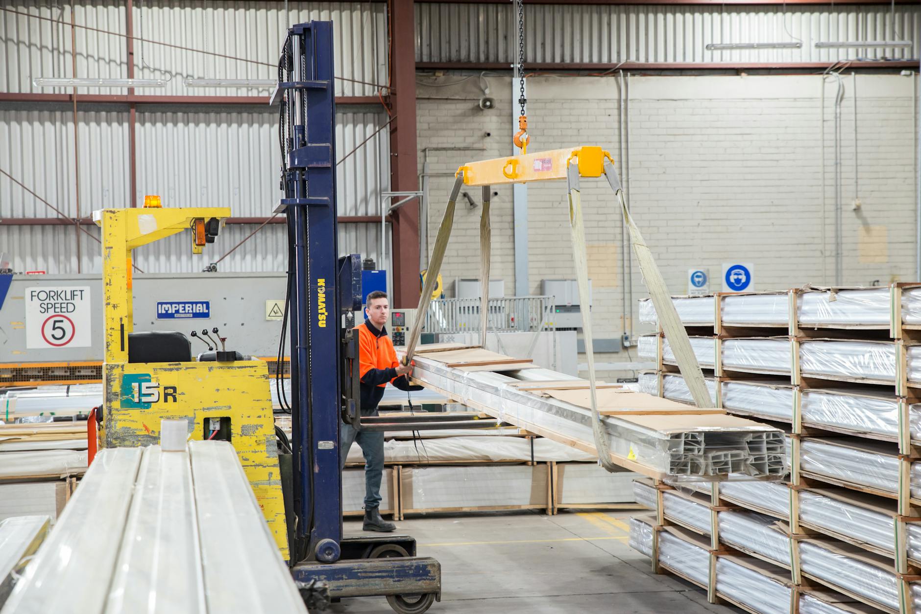 Pracownik manewrujący wózkiem widłowym w magazynie z suwnicą