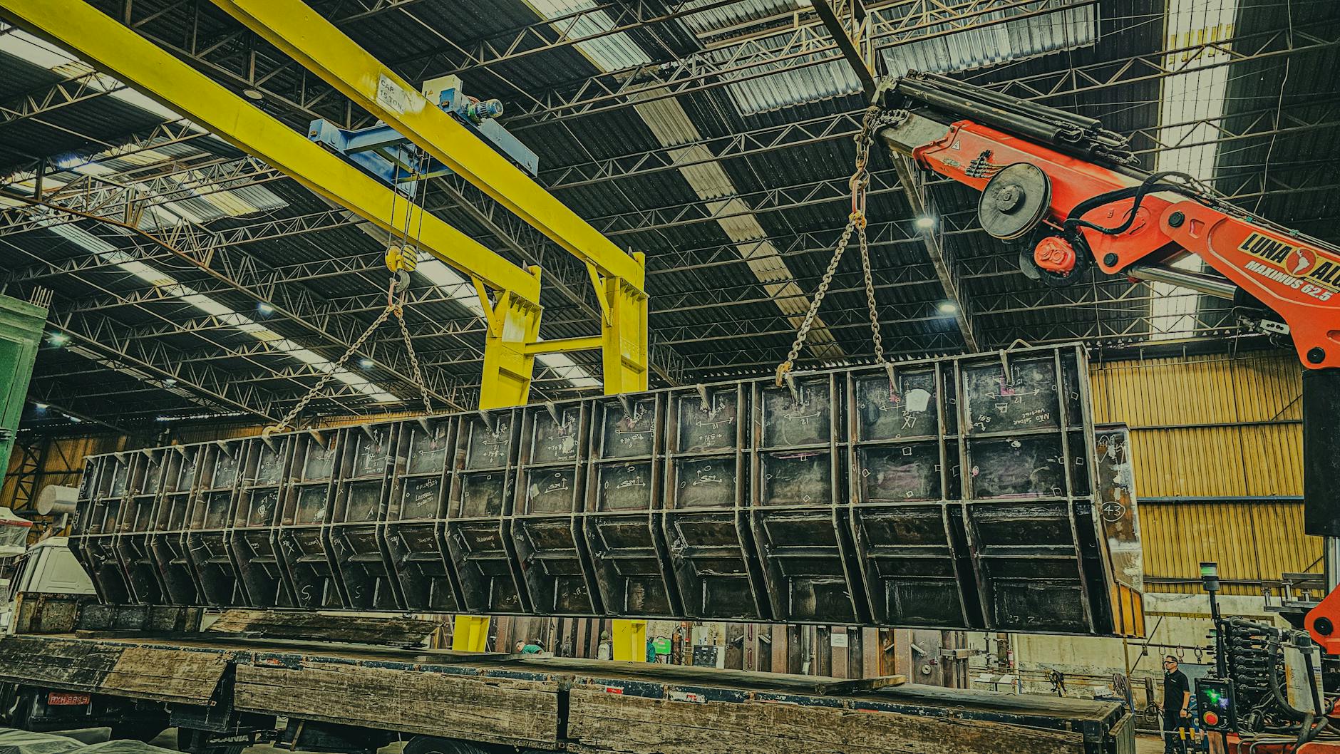 Suwnica przemysłowa podnosi duży metalowy kontener w hali magazynowej