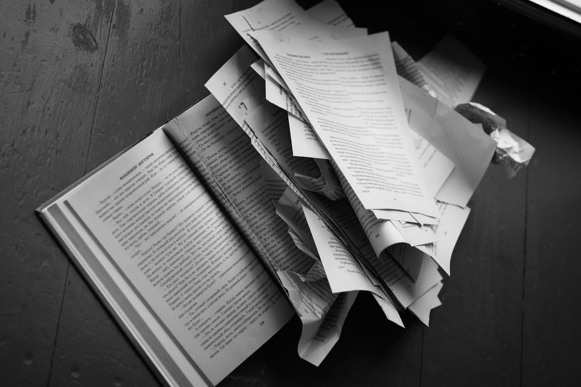 Porwane kartki książki rozsypane na drewnianej podłodze w czerni i bieli Porwane kartki książki rozsypane na drewnianej podłodze w czerni i bieli