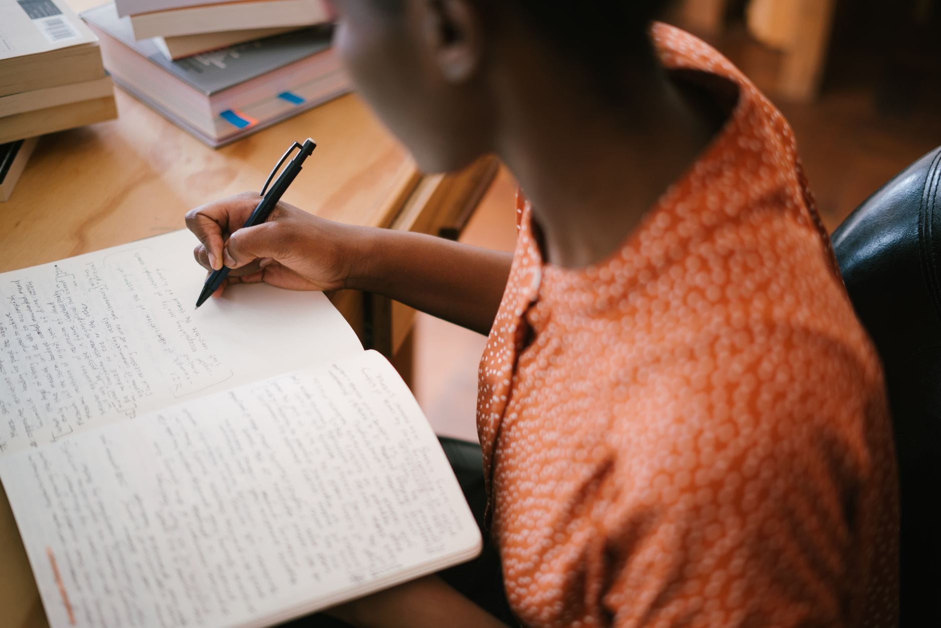 Studentka pisze notatki przy biurku z książkami podczas nauki