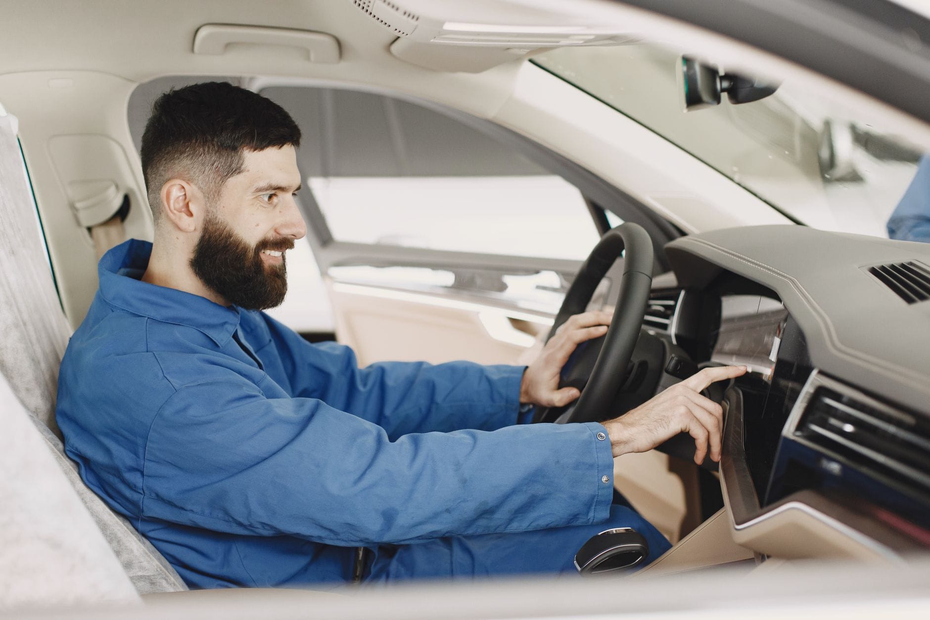 Uśmiechnięty mechanik w niebieskim kombinezonie sprawdza deskę rozdzielczą auta