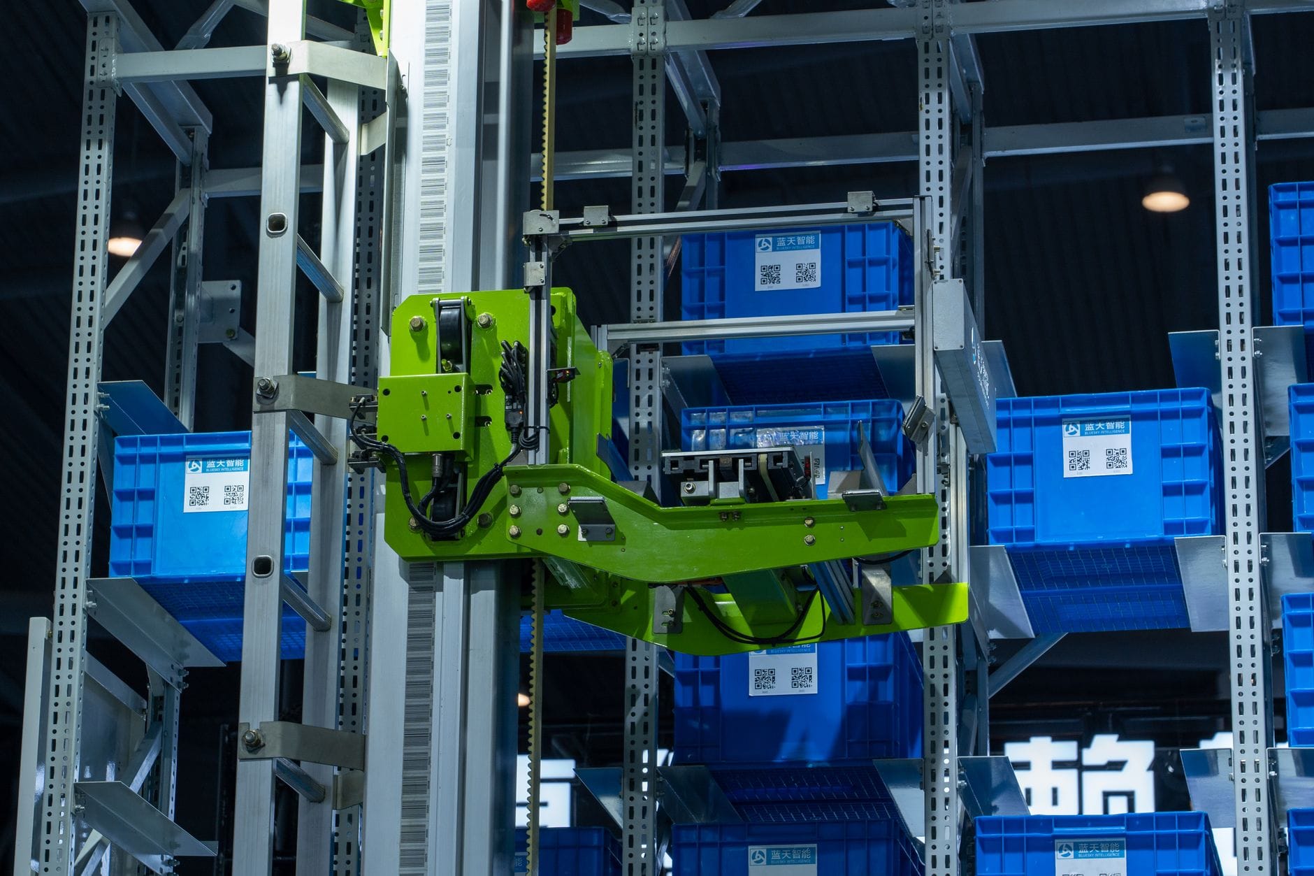 Zielone ramię robota przenoszące niebieskie pojemniki w zautomatyzowanym magazyn