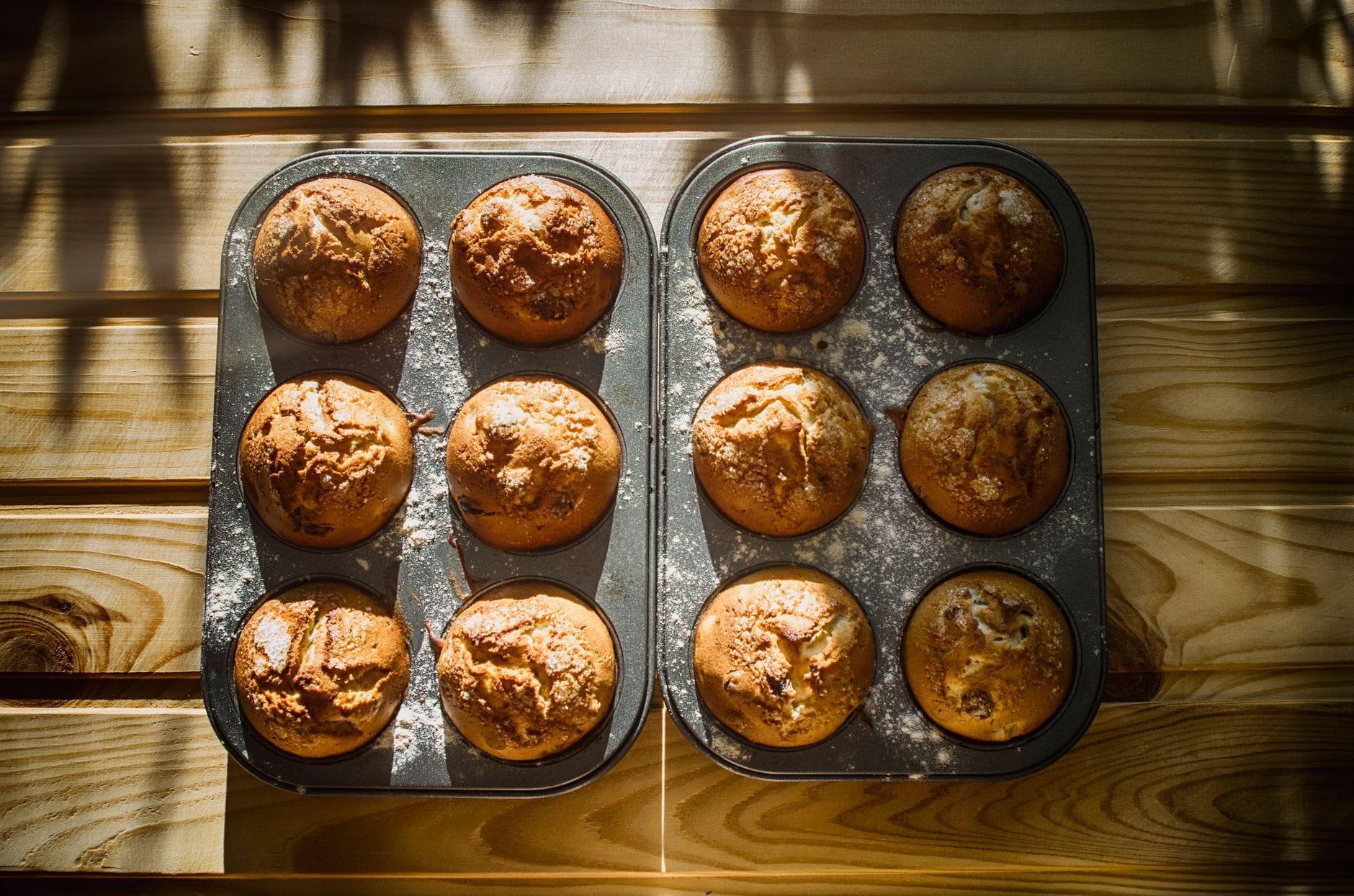 Złote muffiny w metalowej formie na drewnianym blacie w słońcu