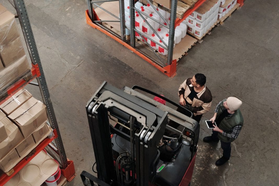 Dwóch pracowników omawia logistykę obok wózka widłowego w magazynie Dwóch pracowników omawia logistykę obok wózka widłowego w magazynie
