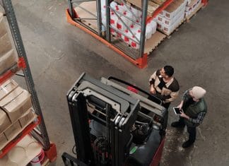 Dwóch pracowników omawia logistykę obok wózka widłowego w magazynie